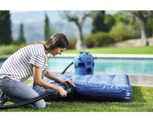 Žena nafukuje matrac elektrickou pumpou v záhrade.