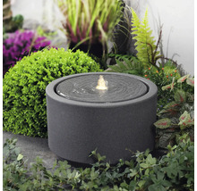 Okrúhla izbová fontána z kameniny s vodnou hrou v záhrade.