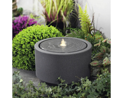 Okrúhla izbová fontána z kameniny s vodnou hrou v záhrade.