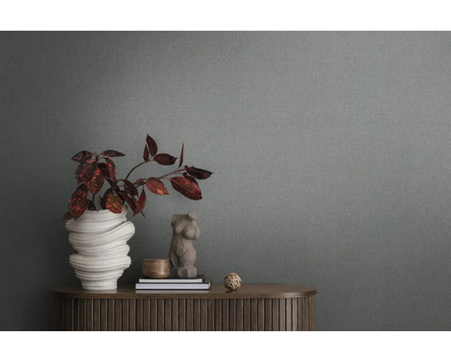 Detailný záber šedej vliesovej tapety so štruktúrou v pozadí miestnosti s komodou a dekoráciou