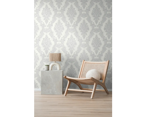 Pohľad do miestnosti s tapetou so vzorom, kreslom a odkladacím stolíkom s lampou a rastlinou