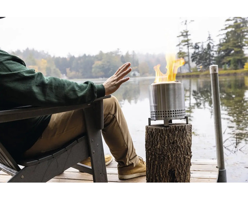 Osoba sa ohrieva pri táboráku na drevenej terase pri jazere.
