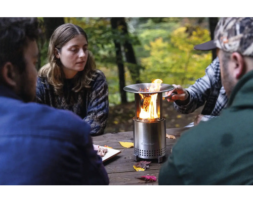 Scéna so skupinou ľudí okolo stola s prenosným ohniskom.