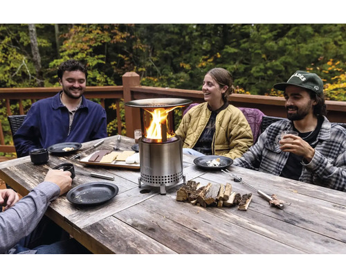 Ľudia sedia pri stole s ohniskom a marshmallows.