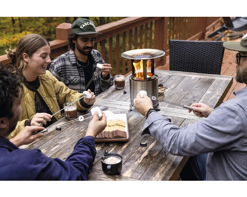 Skupina ľudí opeká marshmallows na vonkajšom stolovom ohni.