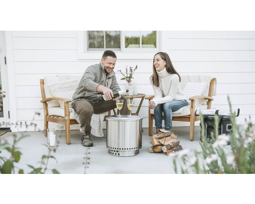 Scéna s párom na terase s ohniskom Solo Stove, drevom a nápojmi.