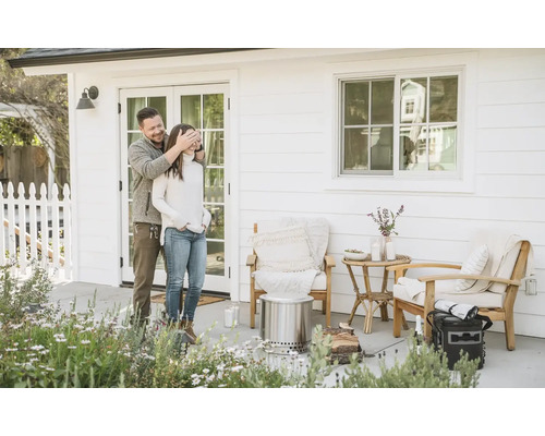 Scéna s párom pred domom s ohniskom, stoličkami a príručným stolíkom na terase