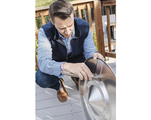 Osoba montuje okrúhle ohnisko striebornej farby vonku.