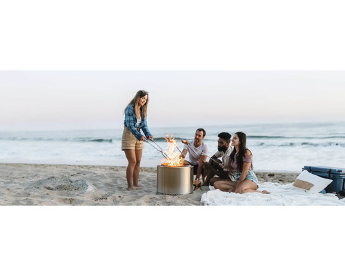 Scéna na pláži so skupinou priateľov sediacich okolo prenosného ohniska a opekajúcich marshmallows