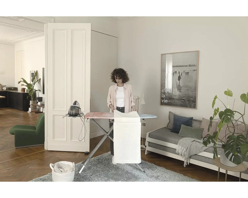 Žena žehlí bielizeň na žehliacej doske s naparovacou žehličkou vo svetlej miestnosti.