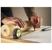 Osoba meria rolku tapety zvinovacím metrom a označuje ju ceruzkou.