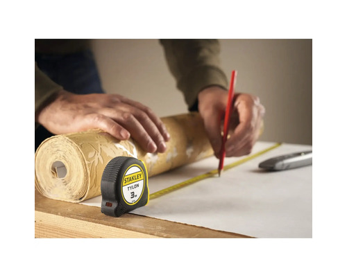 Osoba meria rolku tapety zvinovacím metrom a označuje ju ceruzkou.