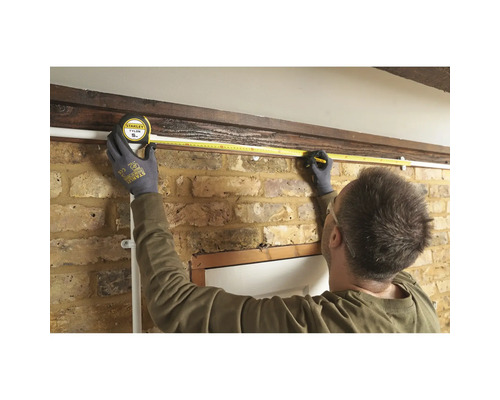 Osoba meria dĺžku steny pomocou zvinovacieho metra.