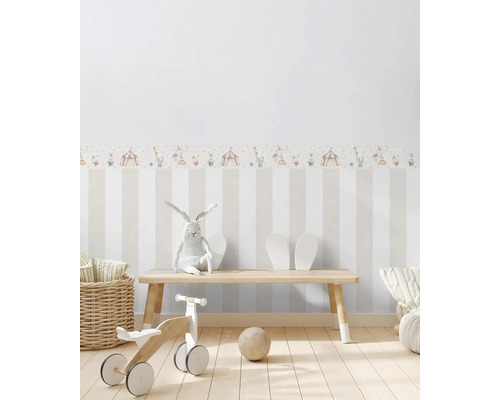 Detská izba s pruhovanou tapetou, cirkusovou bordúrou, hračkami a drevenou lavicou.