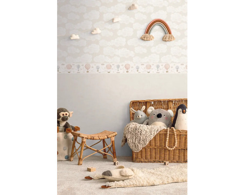 Zdobená detská izba s tapetou s oblakmi, nástennou dekoráciou s dúhou, ratanovou stoličkou a hračkami v košíku.