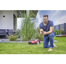 Muž ovláda robotickú kosačku na trávu pomocou smartfónu v záhrade