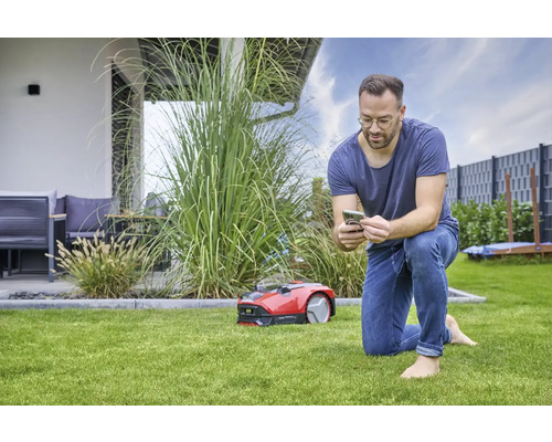Muž ovláda robotickú kosačku na trávu pomocou smartfónu v záhrade