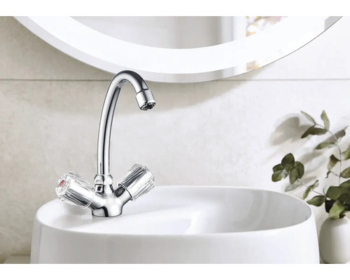 Lesklá vodovodná batéria s priehľadnými rukoväťami na bielom umývadle