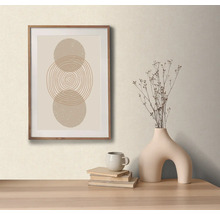 Dekoratívne aranžmán so zarámovaným obrazom s abstraktívnym kruhovým motívom, váza so suchými kvetmi, šálka a knihy na stole.