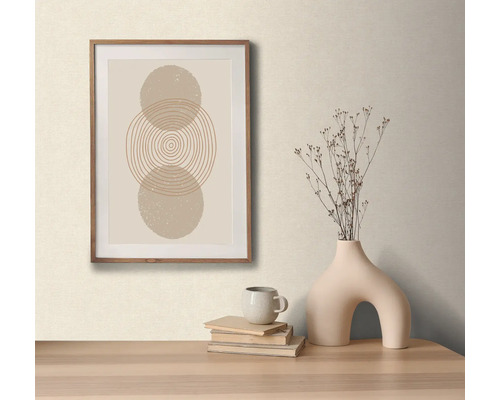 Dekoratívne aranžmán so zarámovaným obrazom s abstraktívnym kruhovým motívom, váza so suchými kvetmi, šálka a knihy na stole.