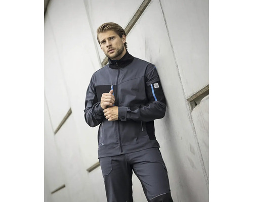 Muž v pracovnej bunde a pracovných nohaviciach pred betónovou stenou