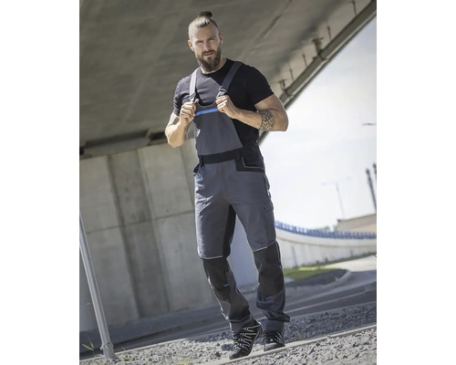 Muž má na sebe sivé pracovné nohavice a čierne tričko pod mostom.