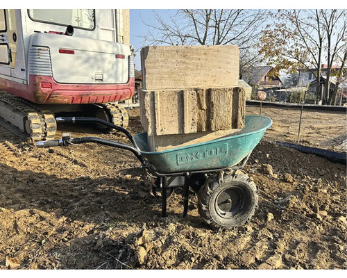 Koliesko s kameňmi a pieskom na pozemku, v pozadí bager.