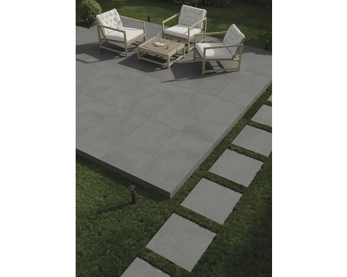 Terasa so sivou dlažbou, sedacia súprava s dreveným rámom a bielymi vankúšmi a šľapáky v trávniku.