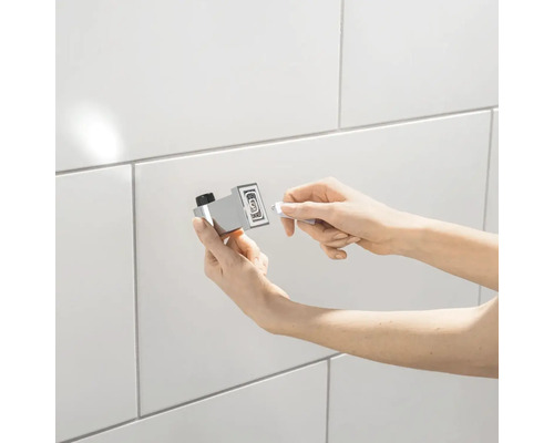 Osoba montuje držiak na uteráky na obkladanú stenu