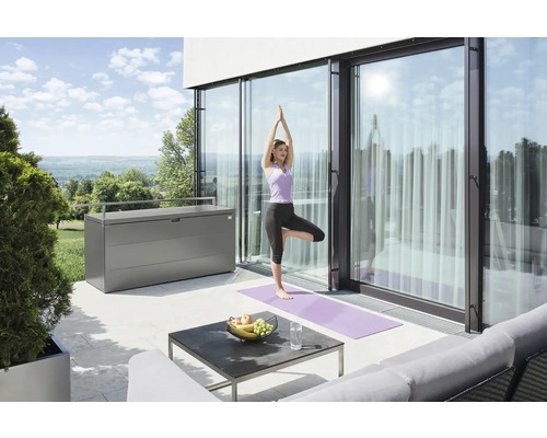 Scéna na terase so ženou cvičiacou jogu, úložným boxom a záhradným nábytkom.