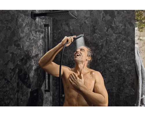 Muž v sprche s hlavovou a ručnou sprchou v kúpeľni s tmavými obkladmi