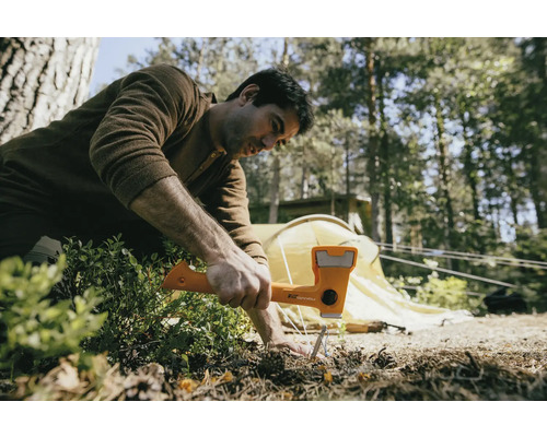 Muž používa kladivo na zatlčenie kolíka do zeme, v pozadí je stan.