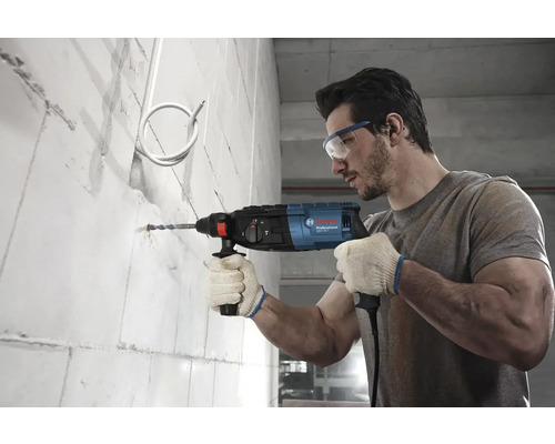 Muž vŕta dieru do steny s príklepovou vŕtačkou Bosch