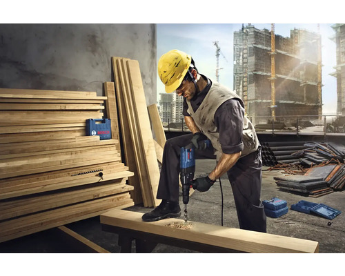 Stavebný robotník vŕta vŕtačkou otvor do drevenej dosky na stavenisku.