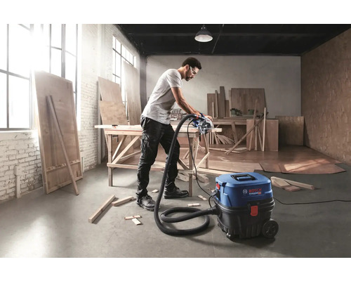 Muž reže dosku kotúčovou pílou, ktorá je pripojená k vysávaču Bosch, v dielni.