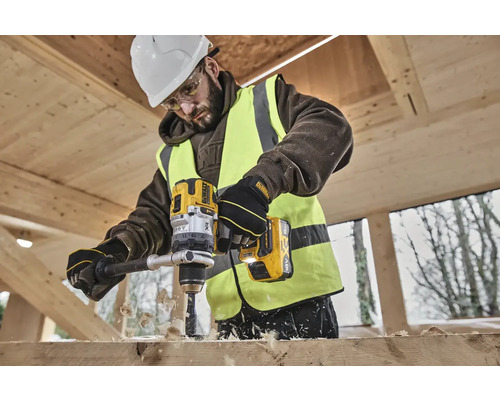 Stavebný robotník vŕta žltou akumulátorovou vŕtačkou DeWalt dieru do drevenej dosky.