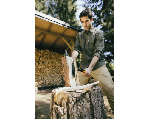 Muž štiepa drevo sekerou na štiepanie na vonkajšom kláte.