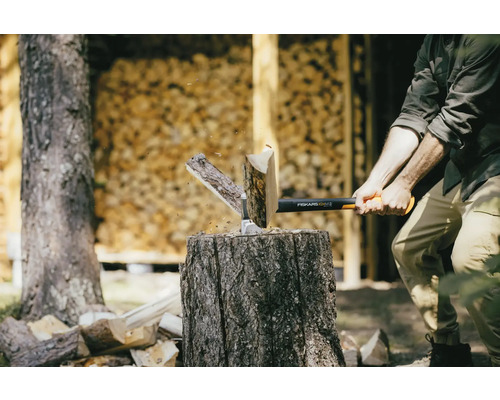 Muž štiepa drevo sekerou Fiskars na kláte