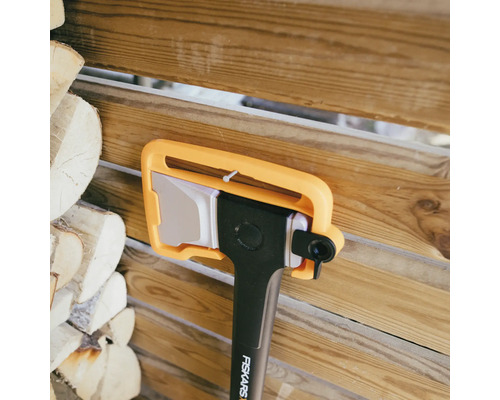 Sekera Fiskars s chráničom čepele pred hromadou dreva