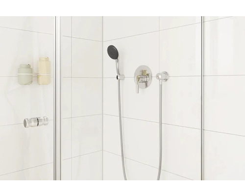 Moderný sprchovací kút s batériou a ručnou sprchou na bielom dlaždicovom pozadí.