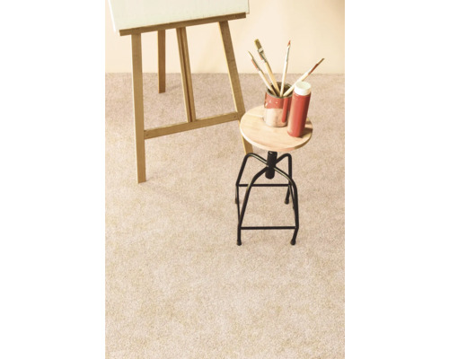 Detailný pohľad na svetlý koberec v ateliéri so stojanom, stoličkou a maliarskymi potrebami.