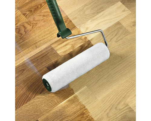 Valček na farbu nanáša farbu na drevenú podlahu.