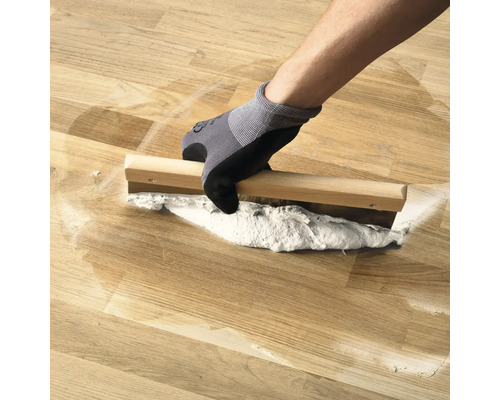 Osoba nanáša drevený tmel na drevenú podlahu pomocou špachtle