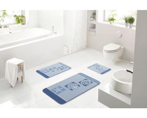 Svetlá kúpeľňa s vaňou, toaletou, umývadlom a súpravou troch modrých kúpeľňových predložiek s námorníckymi motívmi.