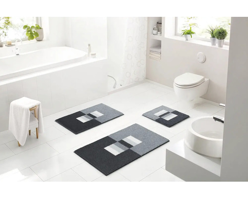 Svetlá kúpeľňa s vaňou, toaletou, umývadlom a trojdielnou sivou súpravou kúpeľňových predložiek s geometrickým vzorom.