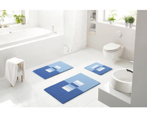 Moderná kúpeľňa s vaňou, toaletou, umývadlom a súpravou troch modrých kúpeľňových koberčekov s geometrickým vzorom