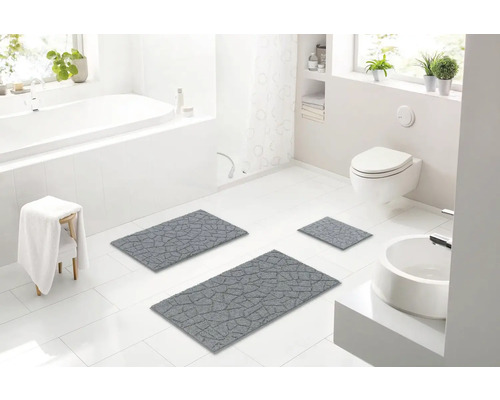 Svetlá kúpeľňa s vaňou, umývadlom, toaletou a sivou súpravou kúpeľňových predložiek.