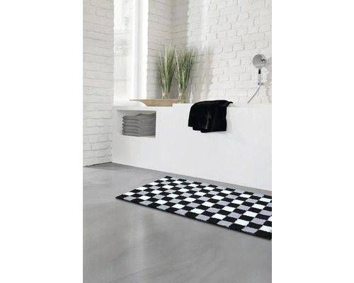 Moderná kúpeľňa s šachovnicovým kúpeľňovým kobercom, bielymi tehlovými stenami a sivými uterákmi.