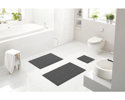 Svetlá kúpeľňa s vaňou, toaletou, umývadlom a tromi sivými kúpeľňovými predložkami.