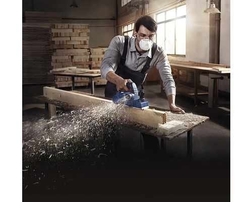 Muž používa elektrický hoblík na drevenej doske v dielni.